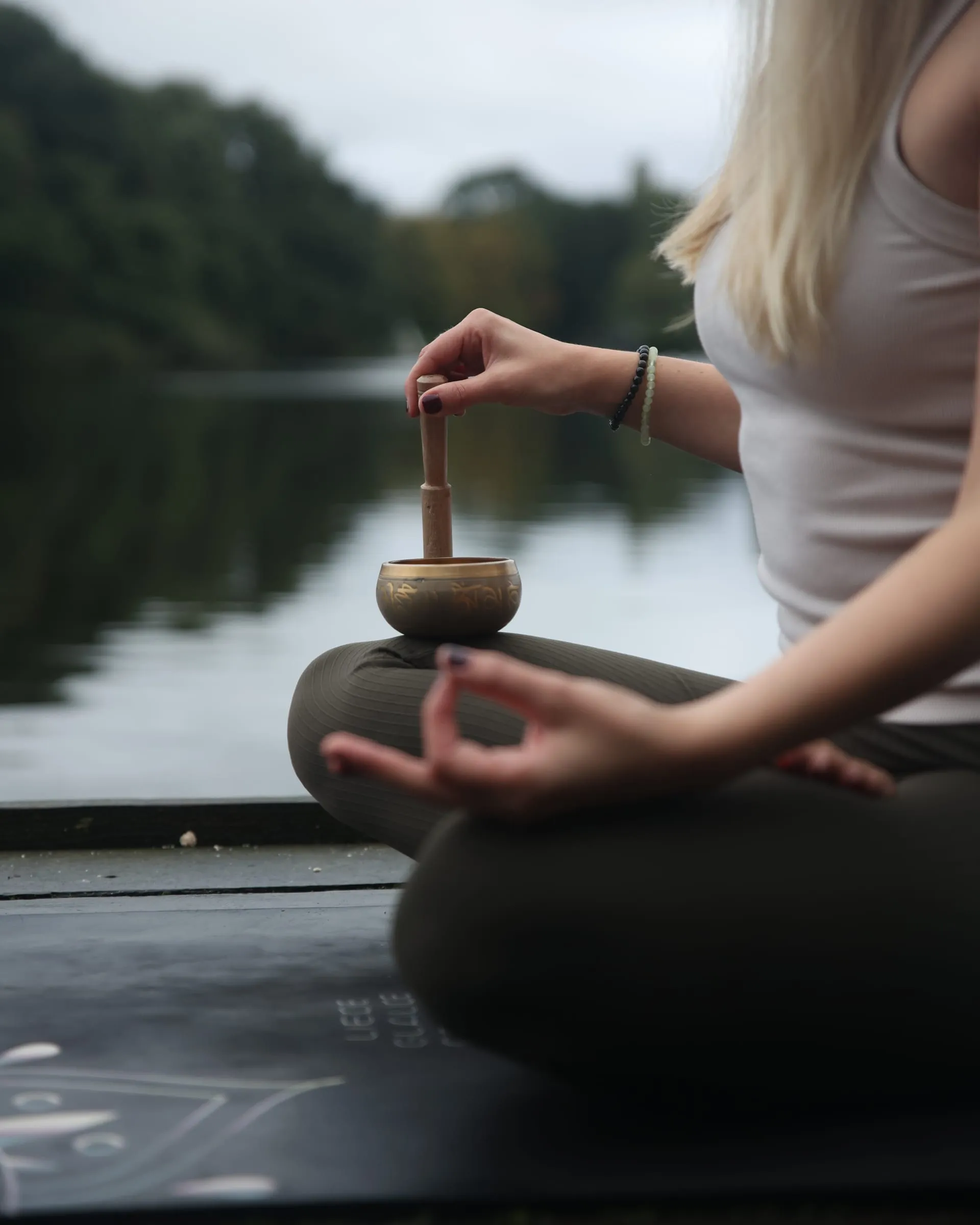 Katrin im Schneidersitz am See, eine Klangschale auf dem Knie, die Hand im Mudra