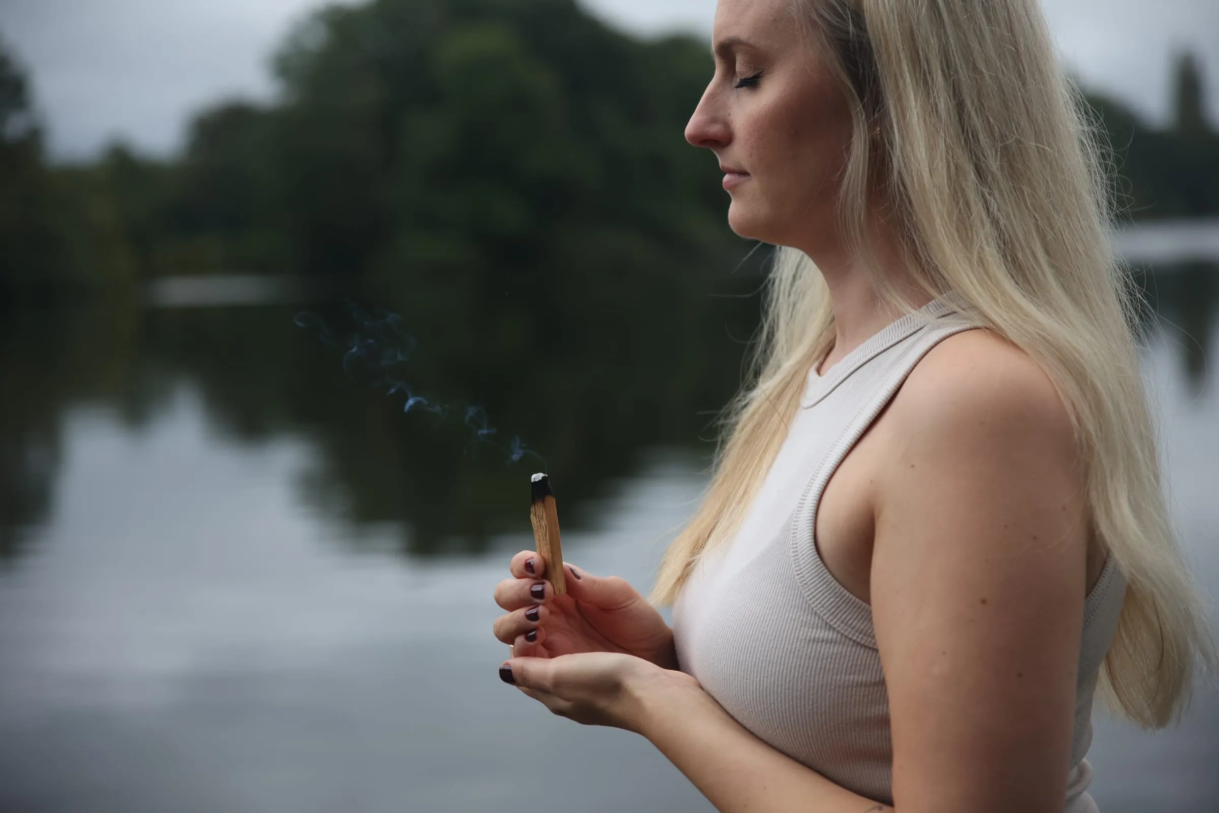 Katrin im Profil mit einem glimmenden Räucherholz vor dem See